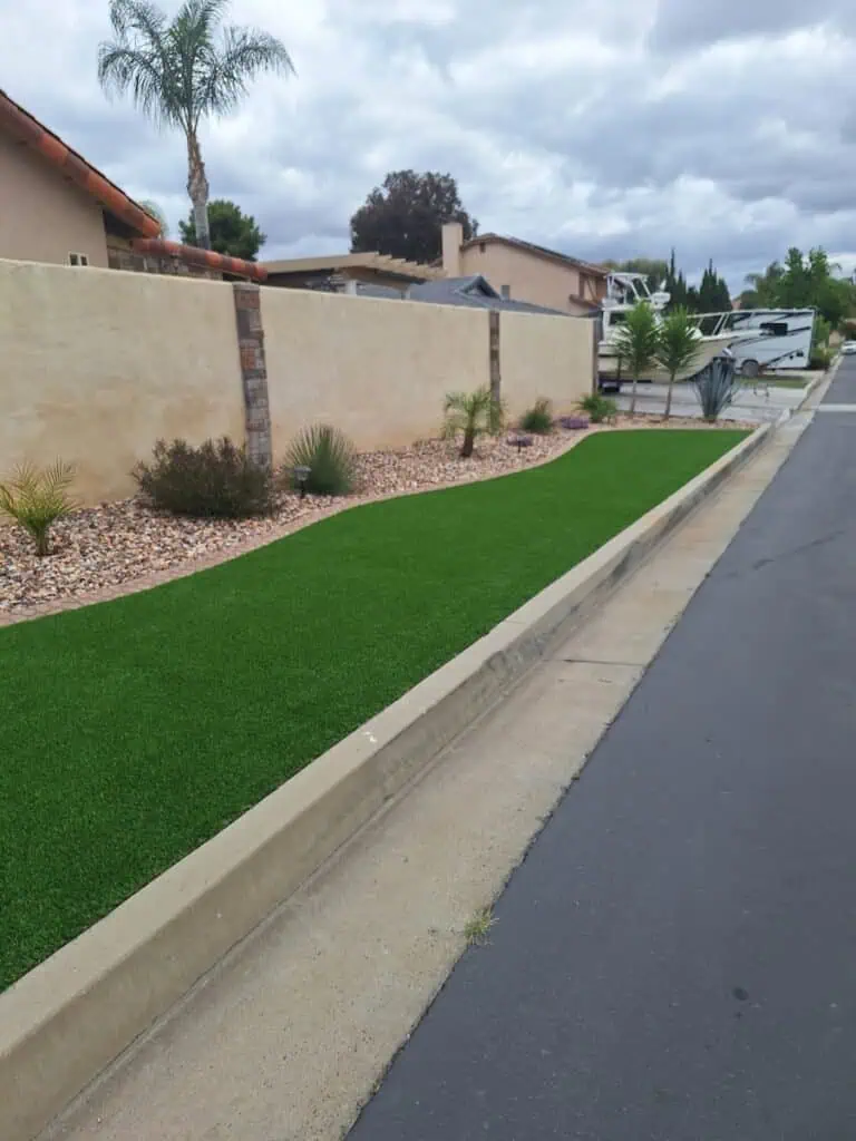 Beautiful lush green lawn with desert plants and decorative rocks along a residential street.